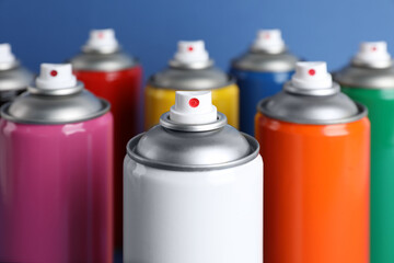 Colorful cans of spray paints on blue background, closeup