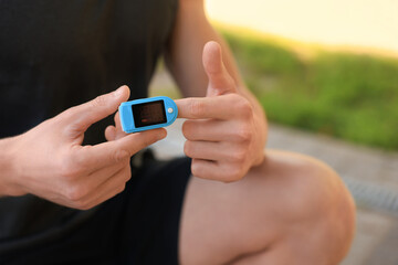Man checking pulse with blood pressure monitor on finger after training outdoors, closeup