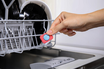 Woman putting detergent tablet into open dishwasher in kitchen, closeup