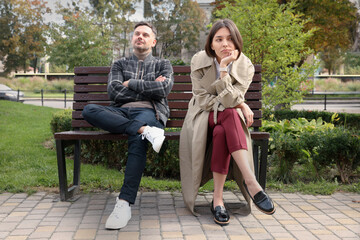 Bored woman sitting near her careless boyfriend on bench outdoors. Relationship problems