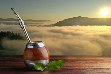 Calabash with mate tea and bombilla on wooden table and beautiful view of mountain landscape, space...