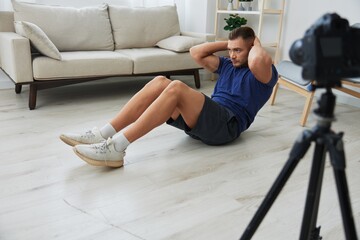 Man athlete blogger records exercise training on the body at home on camera, sports blogger...
