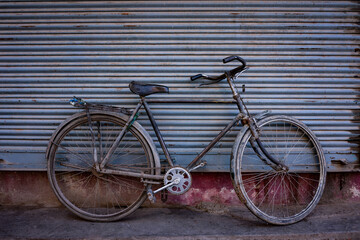 Old rusty bicycle leaning against a closed metal roller gate. Frontal view without people.