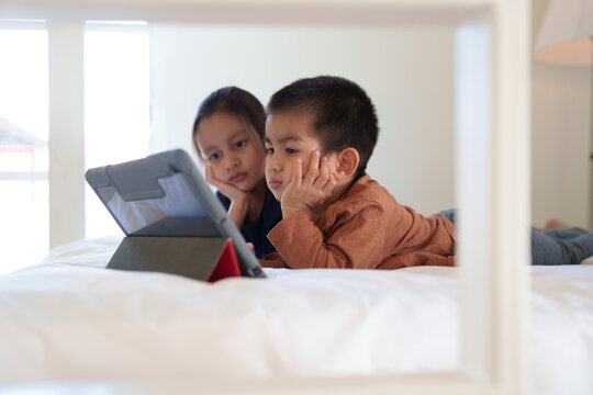 Asian Little Sibling Watching Video Clip On Tablet Together In The Bedroom. Concept Of Technology, Internet, Social Media, Conncection, Learning, Education And Impact To Development, Autism.