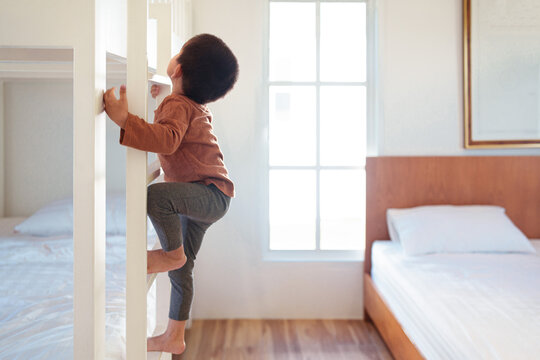 Asian little toddler boy is trying to climb up the ladder of bunk bed in the bedroom. Concept of childhood, kid development, physical activity, muscle, playful, learning, life skill for children.