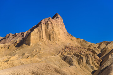 Fototapeta na wymiar Golden Peak - A closeup view of evening sunlight shining on towering Manly Beacon at Badlands, Death Valley National Park, California, USA.
