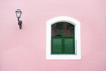 Parede rosa com janela verde e lampião