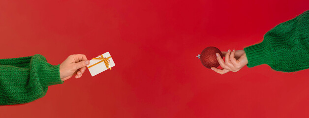 woman's hands in a green sweater hold the symbol of the New Year - a red Christmas ball. Web banner