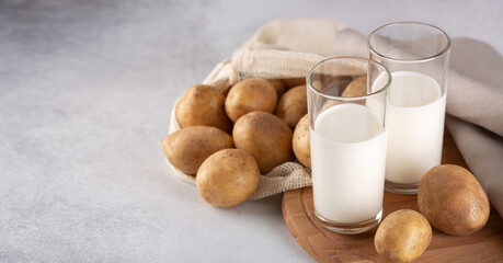 Vegan plant based milk in two transparent glasses. Alternative potato milk and potato tubers on gray table
