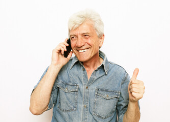 An elderly man dressed in denim shirt holds a smartphone and hears good news.