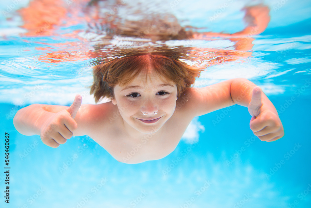 Wall mural Child face underwater with thumbs up. Underwater child swims in pool, healthy child swimming and having fun under water. Water play, healthy outdoor sport activity for children.