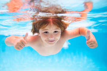 Fototapeta na wymiar Child face underwater with thumbs up. Underwater child swims in pool, healthy child swimming and having fun under water. Water play, healthy outdoor sport activity for children.