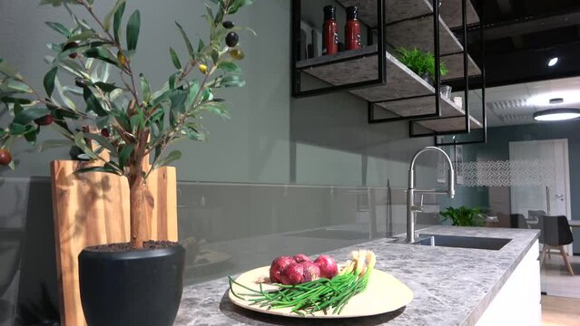 slide shot of potted olive tree, cut board and vegetables on marble countertop with zinc and shelf in the backround