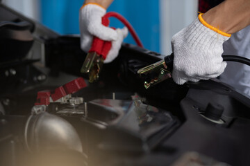 
close up of mechanic Tow the car battery when facing dead batteries in the garage. battery extension cable car maintenance service concept