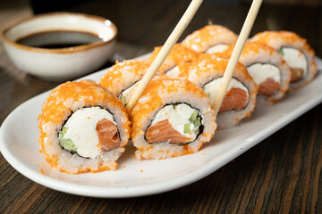 closeup of sushi rolls with chopsticks on white plate.