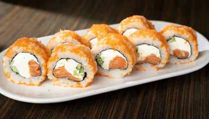 Japanese food California maki sushi with salmon, cucumber and flying fish roe on plate and background.