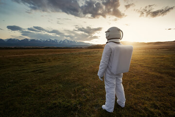 An astronaut explores an unknown planet. Sunset sky and mountains in the background.