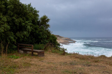 A bench with a beautiful view of the ocean with waves in cloudy weather and clouds.