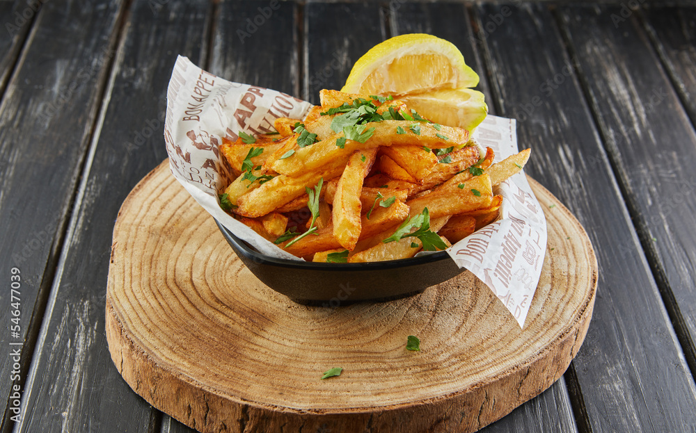 Wall mural Potatoes with parsley and lemon, fried in oil on wooden board, serving in cafe