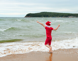 Child boy in red cloth and Santa Claus hat enjoying Christmas on the beach on Xmas travel vacation. Christmas or New Year celebration concept