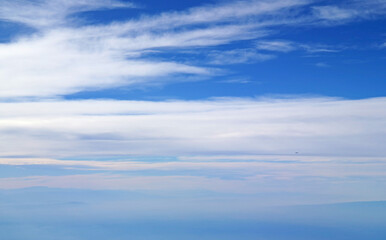 Vivid blue sky and white spreading clouds with an airplane flying in distance view during the flight