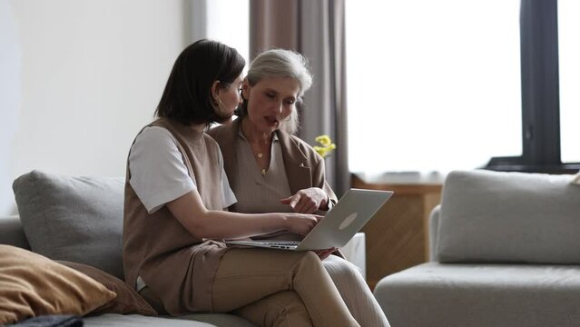 adult mother with daughter watching funny videos at home on laptop