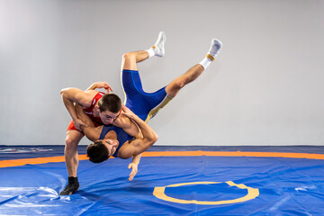 Two young men in blue and red wrestling tights are wrestlng and making a suplex wrestling on a...