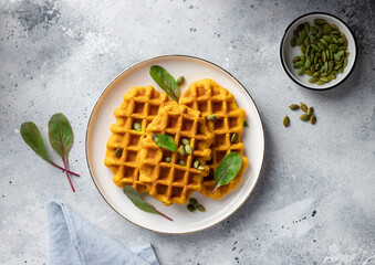 Pumpkin Belgian waffles with seeds and greens on gray background. Plant based diet concept. flat lay
