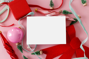 Christmas card mockup, pink flat lay. Empty card with space for text and red bow, little trees, baubles, ribbons on pink background. Modern creative template, seasons greetings © sonyachny