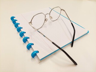 Chrome and black reading glasses on blue, open booklet notebook on white background white desk in office. Image taken in Belgium, Leuven.