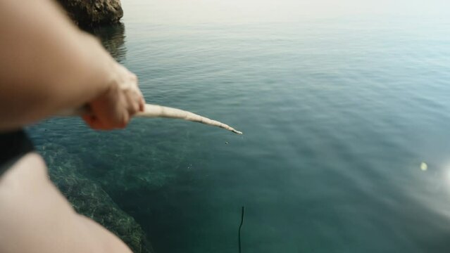 A girl in a swimsuit is fishing in the sea with a homemade bamboo fishing rod, Clear water, the float is sinking.