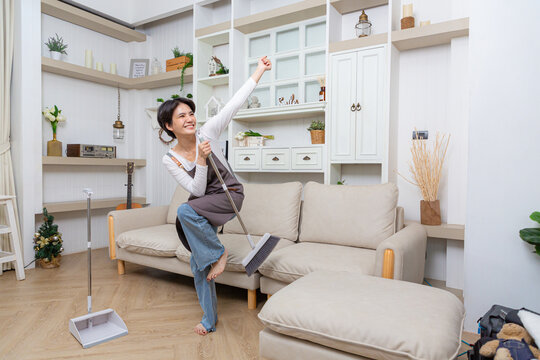 Happy asian woman holding with mop cleaning floor and singing at home. Housekeeping concept