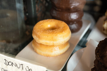 An original glazed donut or doughnut pieces which are place on white ceramic dish. Close-up and selective focus.