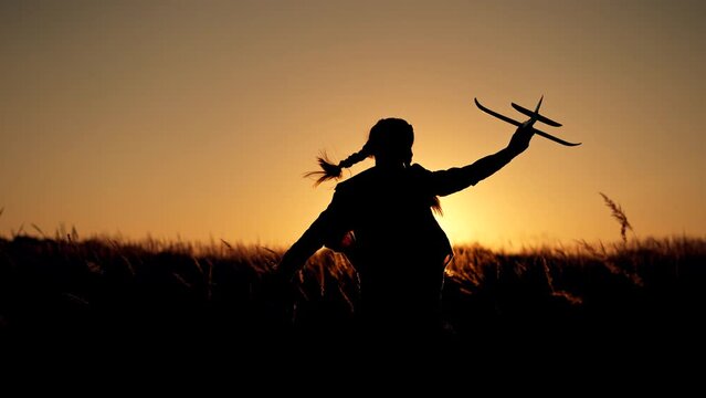 Happy girl with oy in natural park. Child runs on grass with an airplane. Chidhood dream. Happy baby girl with toy airplane at sunset. Child runs on grass in field. Dream travel concept