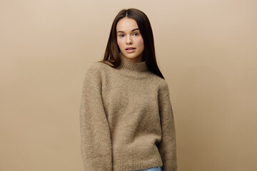 horizontal photo of a beautiful, attractive, relaxed woman in a warm, textured, autumn sweater looking pleasantly into the camera standing on a beige background