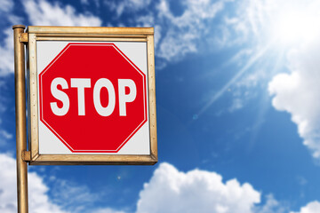 Close-up of a stop road sign against a clear blue sky with clouds and sunbeams, photography.