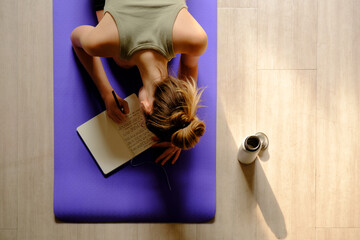 Overhead image of Young caucasian woman making a journal entry while sitting on a yoga mat.