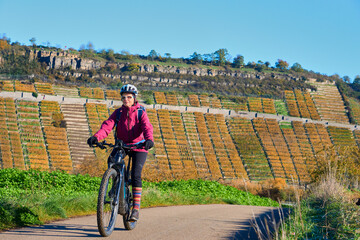 nice senior woman riding her electric mountain bike in the steep autumnal colored vineyards of...