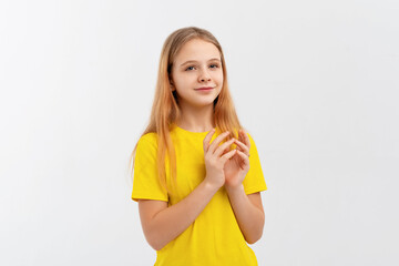 Lovely teen girl in yellow t-shirt, rubs hands and smiles, relish smth good, applause, looks happy, stands over white background