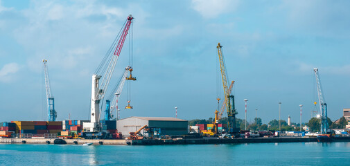 cargo sea port with cranes, container stacks and trucks with goods, sea hub terminal from seashore