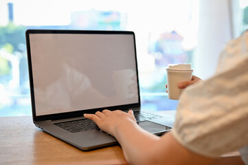 Asian female remote working at the coffee shop, using laptop while sipping coffee.