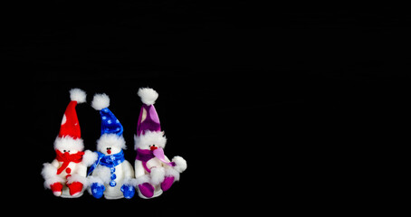 Fototapeta na wymiar Banner with three handmade toy snowmen with hats and scarves on a black background. Christmas and New Year concept