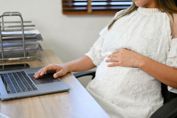 Beautiful Asian pregnant businesswoman working at her desk, using laptop. cropped shot