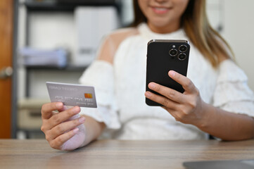 Asian businesswoman sitting at her desk holding a credit card and her smartphone. cropped shot
