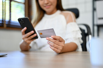 Asian businesswoman sitting at her desk holding a credit card and smartphone. pay online bills.