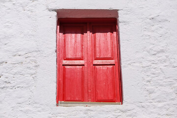 Window with bright red closed shutters on a white wall