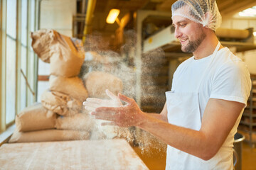 Junger Mann als Bäcker Lehrling klatscht Mehl von den Händen