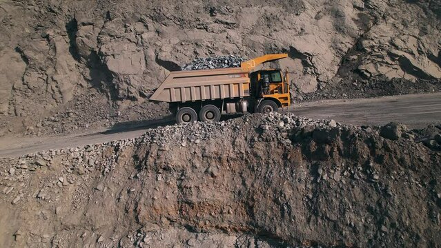 Large yellow dump truck loaded with rock is driving uphill along a quarry towards empty dump truck in a general view. Big heavy mining truck driving across the work site