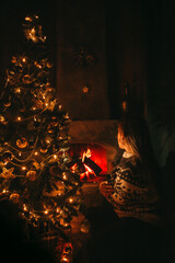 Woman Decorating the Christmas tree with golden decorations on it next to the fireplace. Christmas Eve concept. 