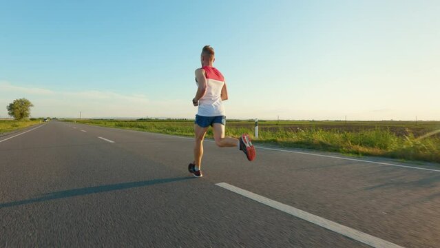Back view of sportsman exercising, training, working out, running in hot summer. Athlete taking part in marathon, wearing shorts and T-shirt. Concept of sport and healthy lifestyle.